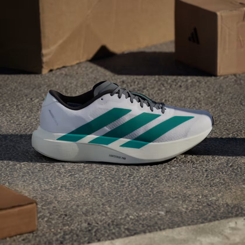 Adidas running shoe with green stripes on a concrete surface with cardboard boxes in the background