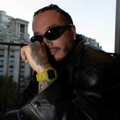 J BALVIN wearing G-SHOCK watches, sunglasses and a black leather jacket with a cityscape background