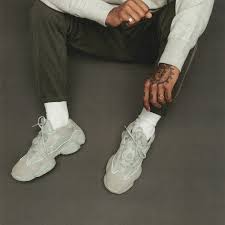 Person wearing Men's Adidas Yeezy 500 - Stone Salt sneakers on a dark background
