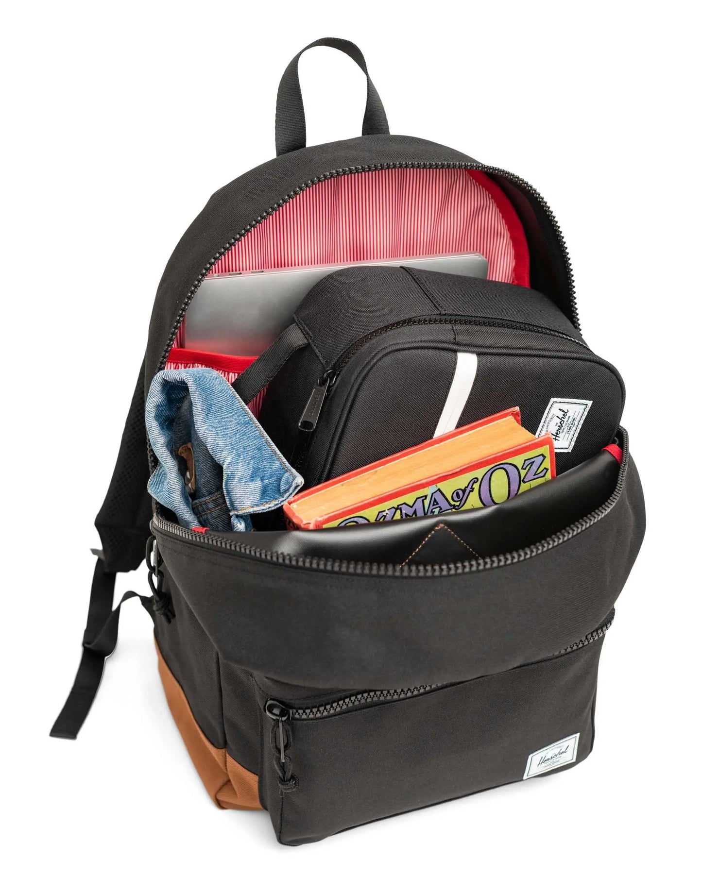 Black backpack with various items including a book titled 'The Wonderful Wizard of Oz' on a white background