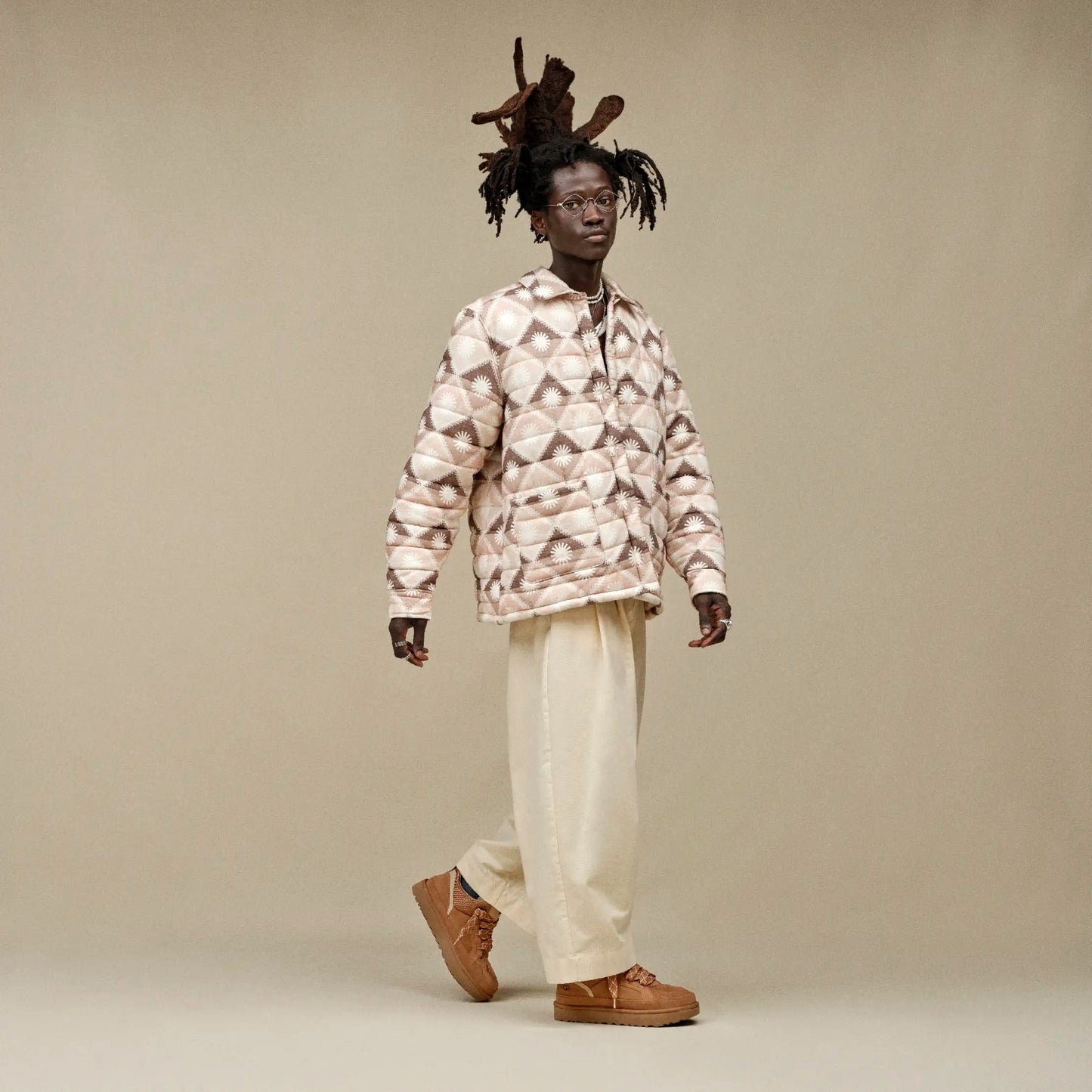 Person wearing a patterned shirt and beige pants on a plain background