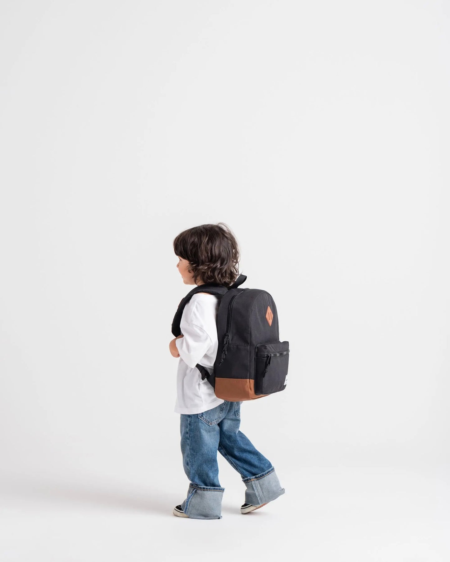Child wearing a black backpack with a brown patch on a white background