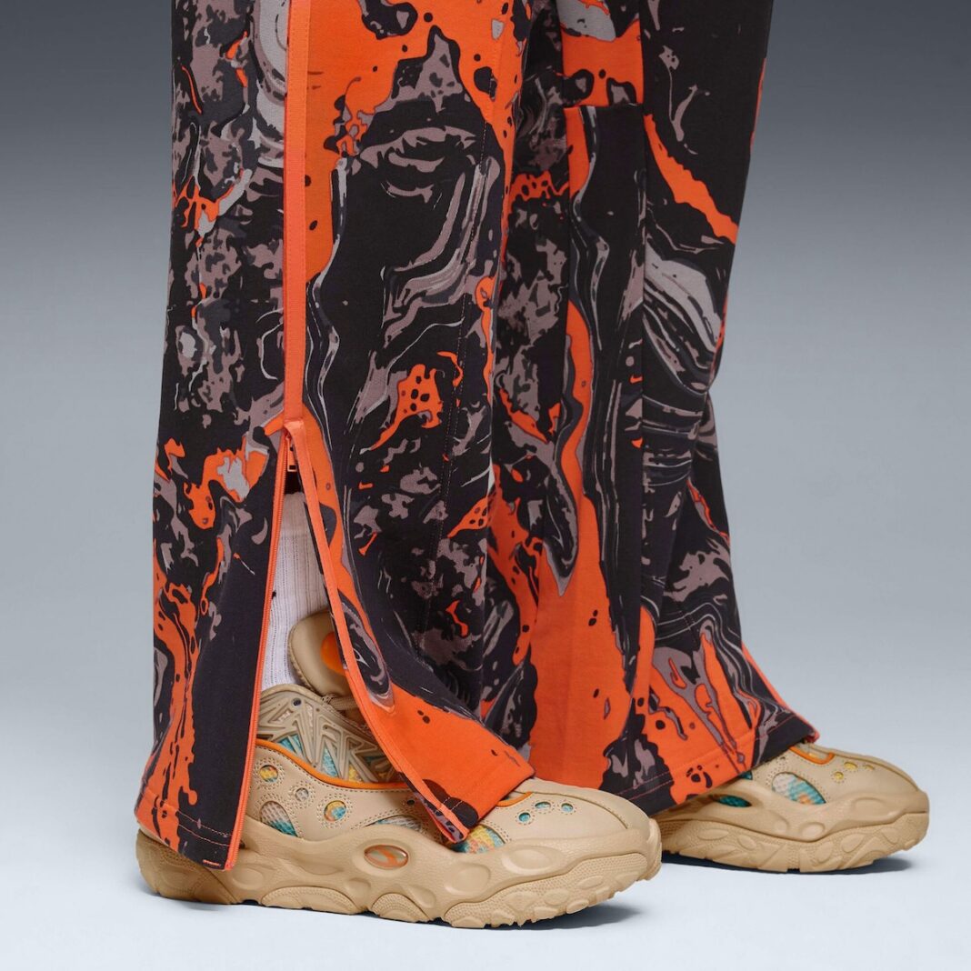 Colorful pants with orange and black patterns worn with beige sneakers on a gray background