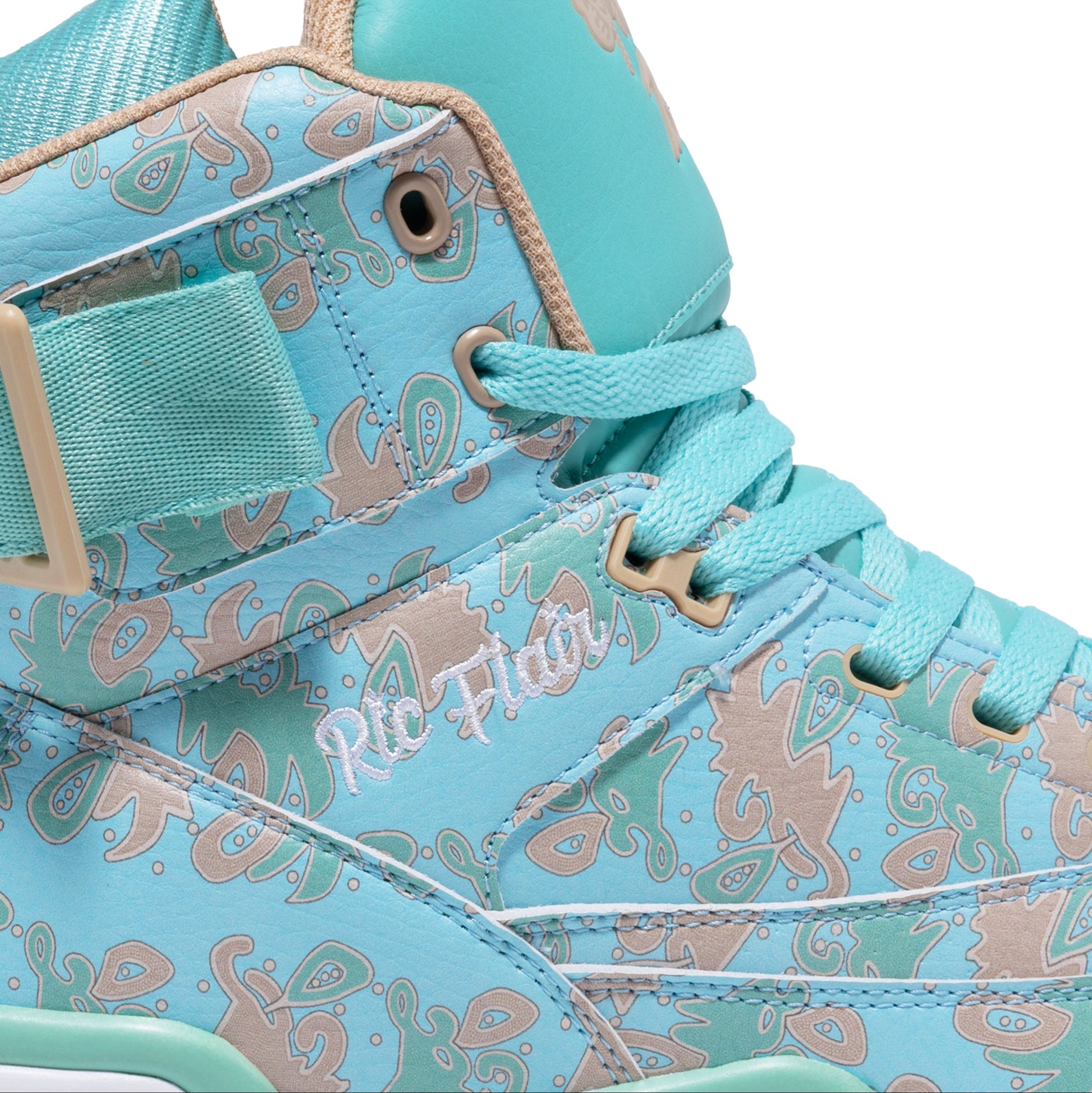 A close-up of a high-top sneaker in light turquoise blue with a beige and brown paisley pattern, featuring a hook-and-loop strap on the side and the text 'Ric Flair' printed on the side panel.