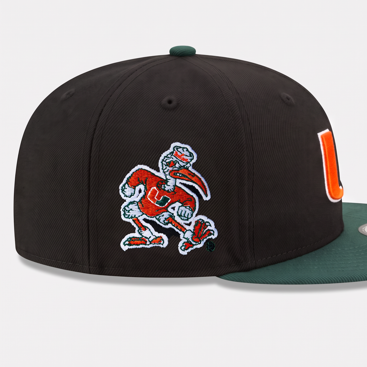 A black structured baseball cap featuring an embroidered Miami Hurricanes mascot patch on the front and a green flat brim, shown against a light gray background.