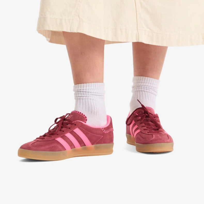 Person wearing pink Adidas sneakers with white socks on a plain background