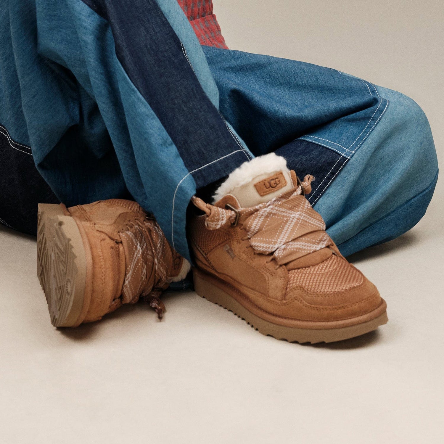Brown lowmel UGG boots with white fur lining worn with blue jeans on a neutral background