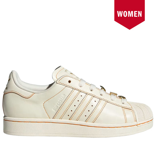 White sneaker with gold accents on a white background, featuring a 'WOMEN' label.