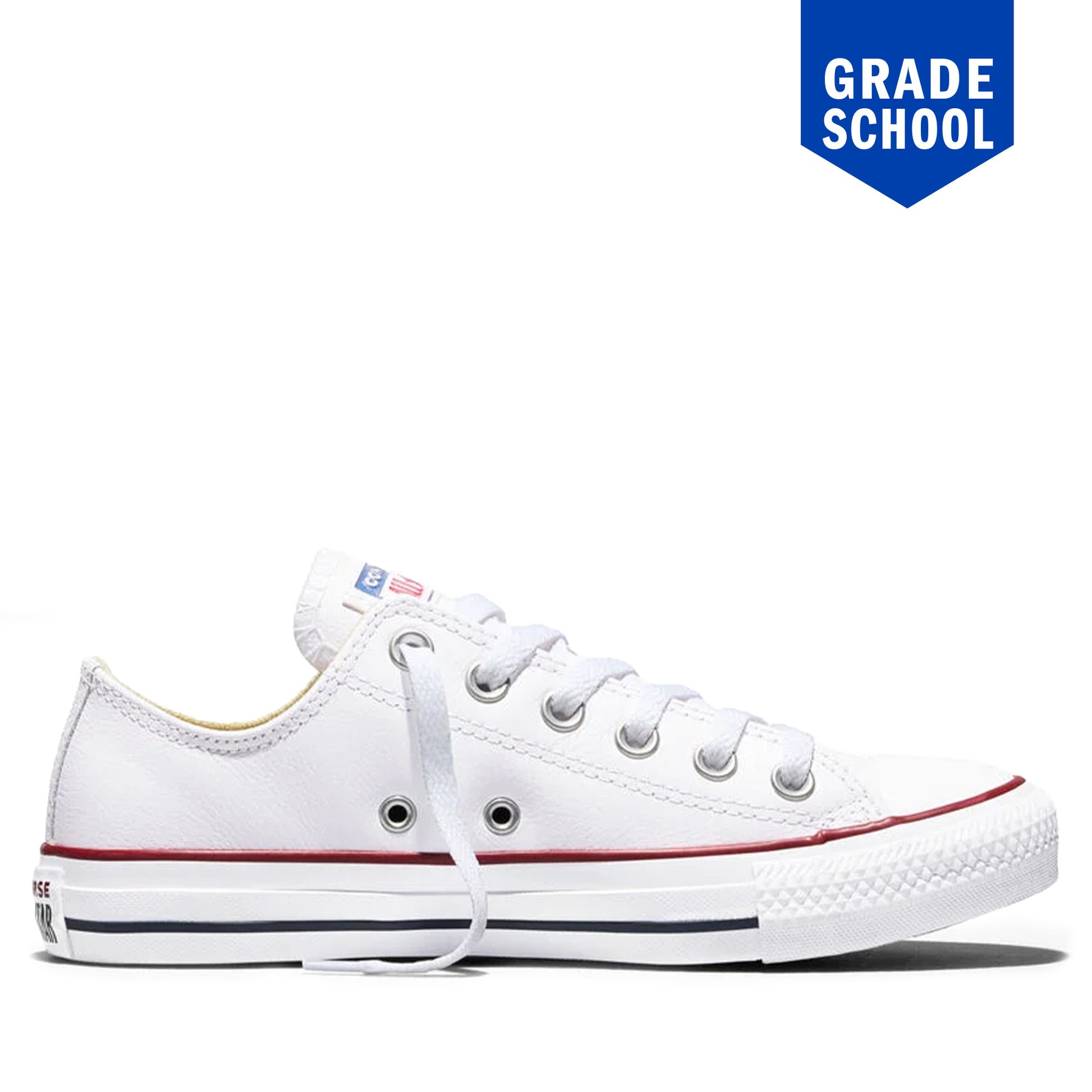 A white low-top canvas sneaker with white laces, a red stripe along the side, and a black stripe along the sole, shown on a white background with a blue 'GRADE SCHOOL' badge in the top right corner.