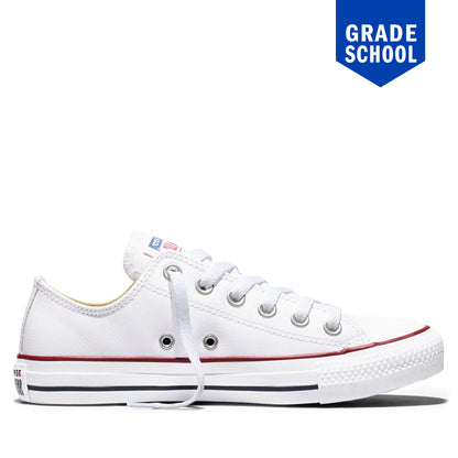 A white low-top canvas sneaker with white laces, a red stripe along the side, and a black stripe along the sole, shown on a white background with a blue 'GRADE SCHOOL' badge in the top right corner.