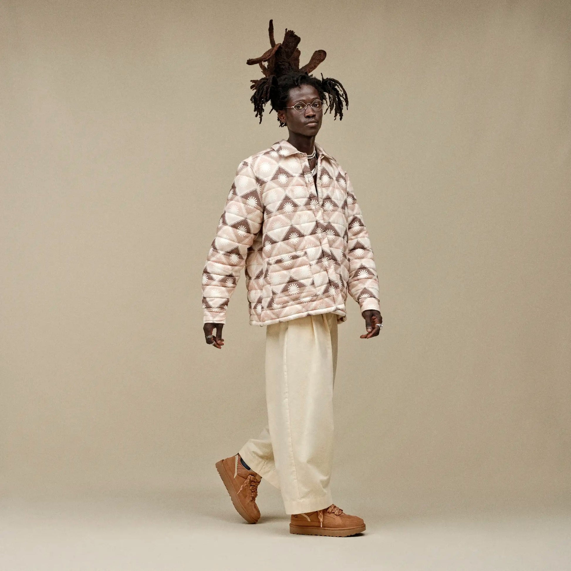 Person wearing a patterned shirt and beige pants on a plain background