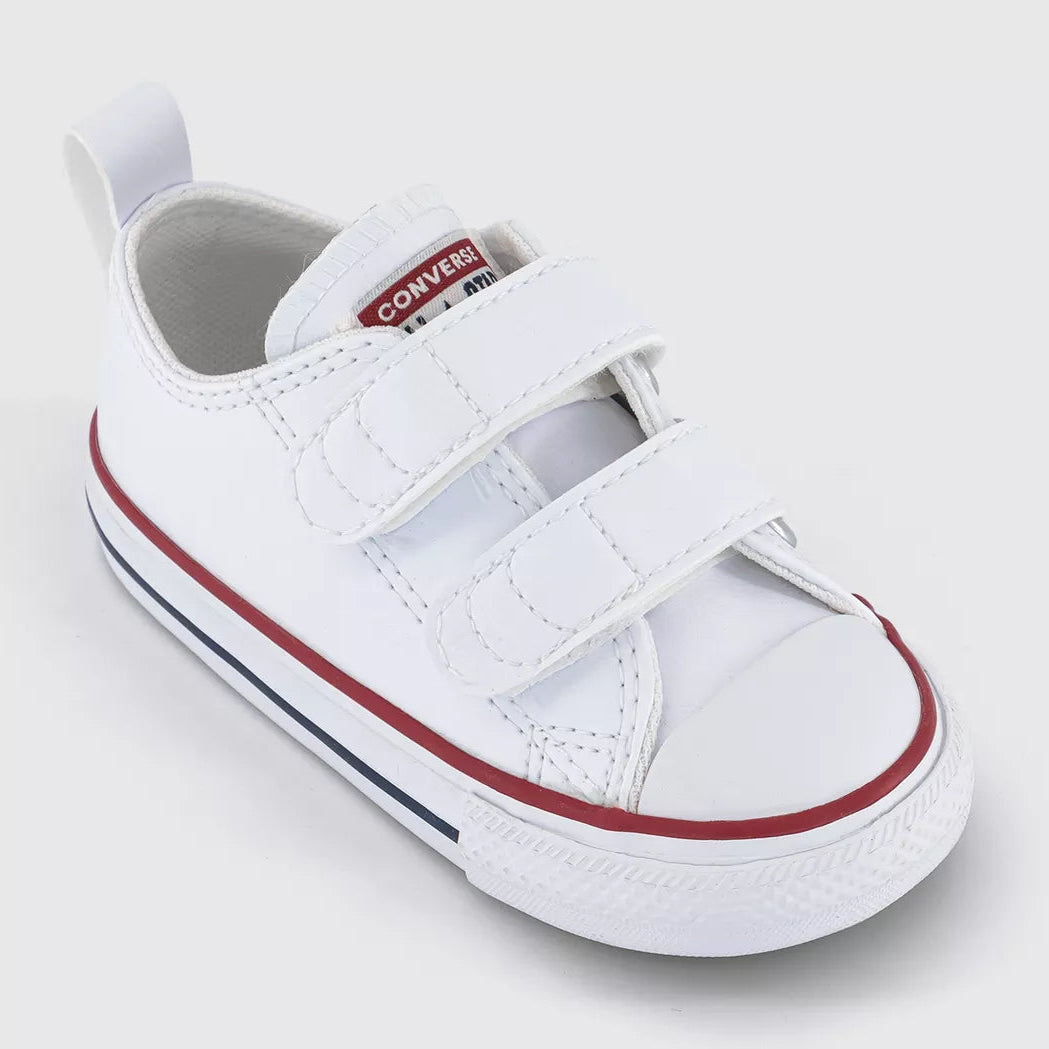A white baby bootie sneaker with two hook-and-loop straps, featuring a red stripe along the side and a red and white Converse logo on the tongue, set against a light gray background.
