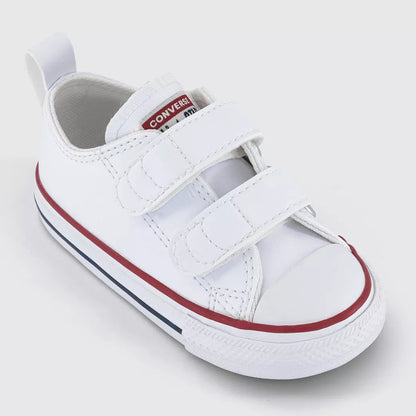 A white baby bootie sneaker with two hook-and-loop straps, featuring a red stripe along the side and a red and white Converse logo on the tongue, set against a light gray background.