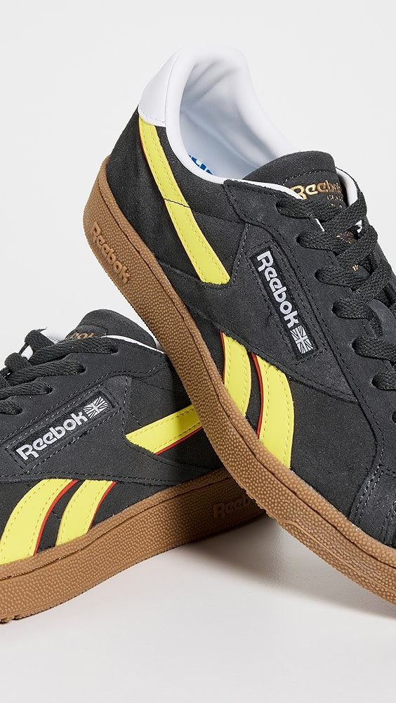Black Reebok sneakers with yellow and brown accents on a light gray background