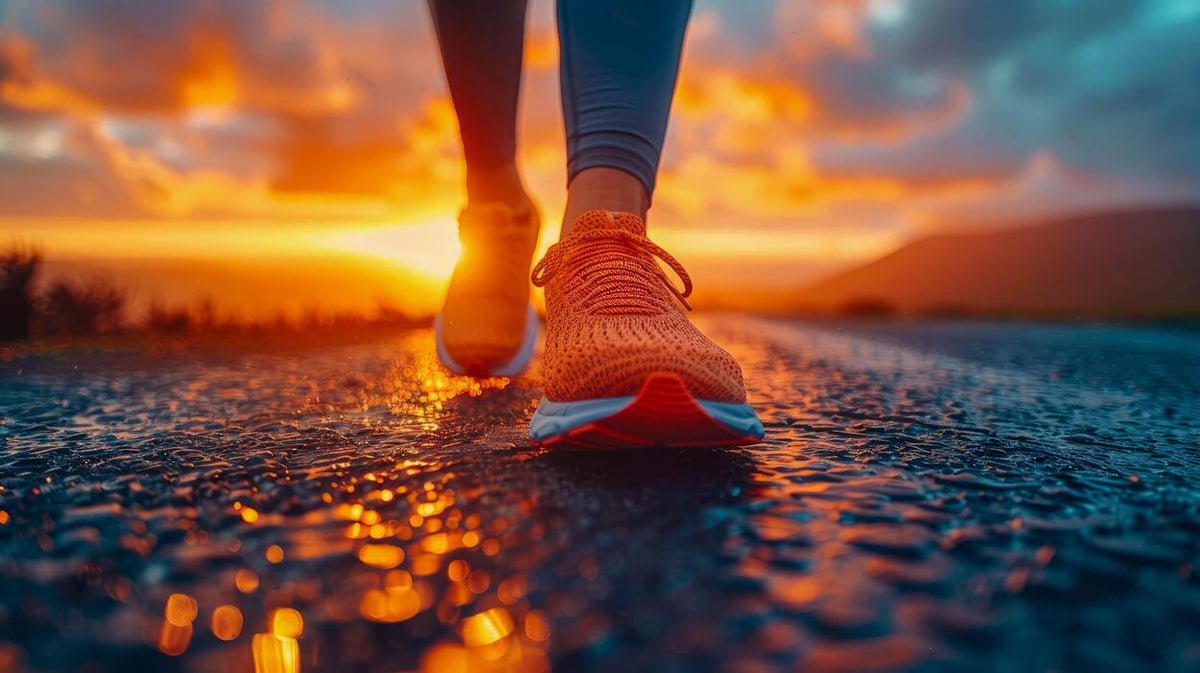 A close-up action shot of a runner's feet wearing orange knit running shoes and blue leggings, walking on a wet road during a dramatic orange sunset.