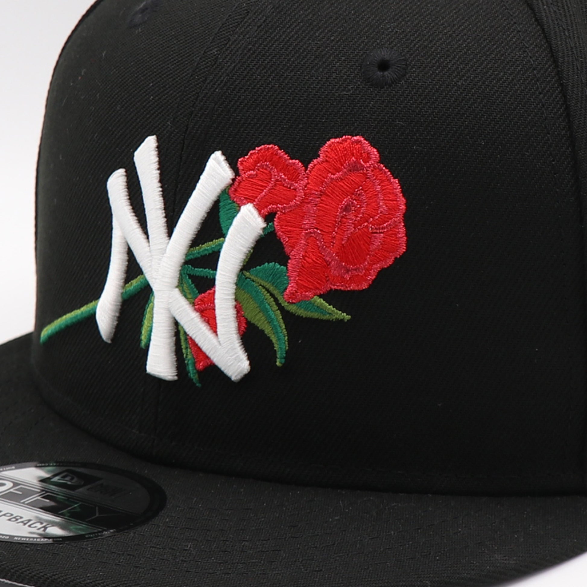 Black cap with embroidered design of roses and letters on a white background