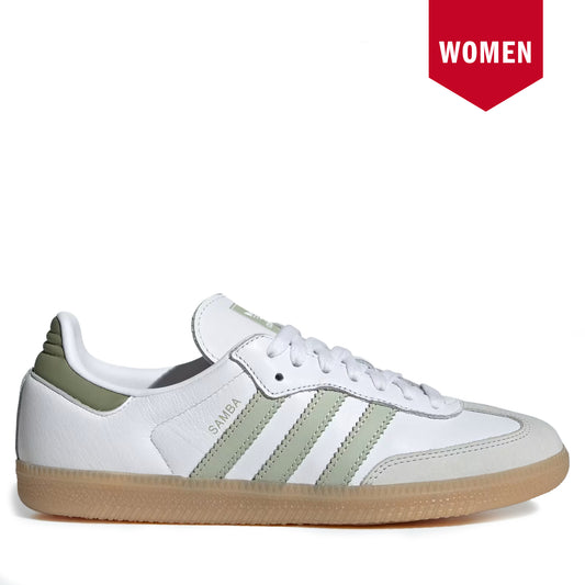 A white Adidas Samba sneaker with sage green stripes and heel tab, featuring a gum sole, shown against a white background with a red 'WOMEN' badge in the top right corner.